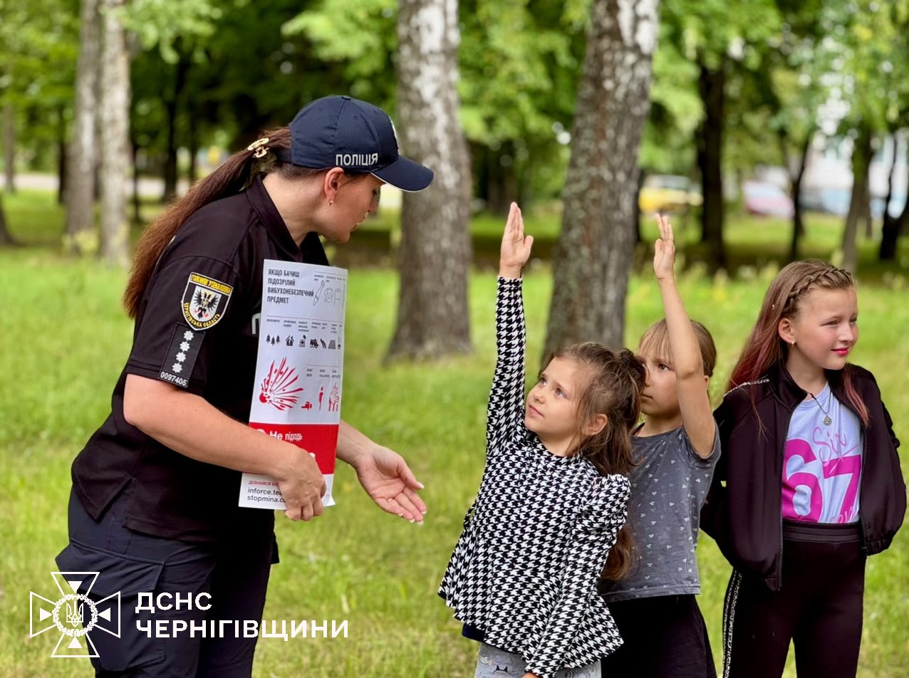 Фотографія на тлі літнього парку поліцейська говорить з дітьми, діти піднімають руки